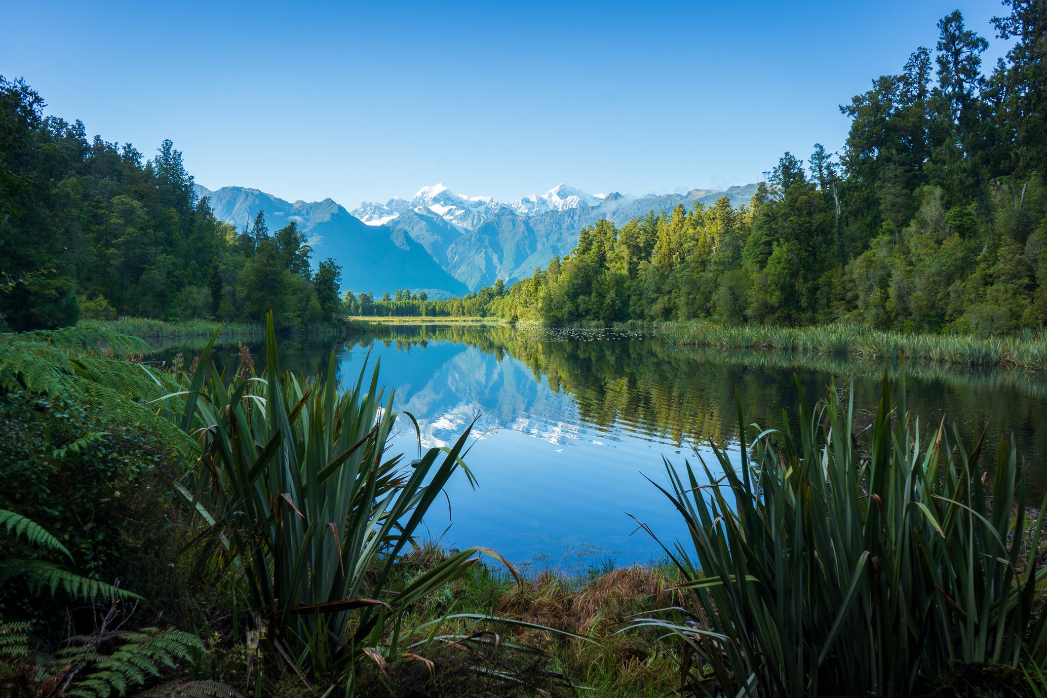 Tranquil lake reflecting snow-capped mountains and lush greenery.