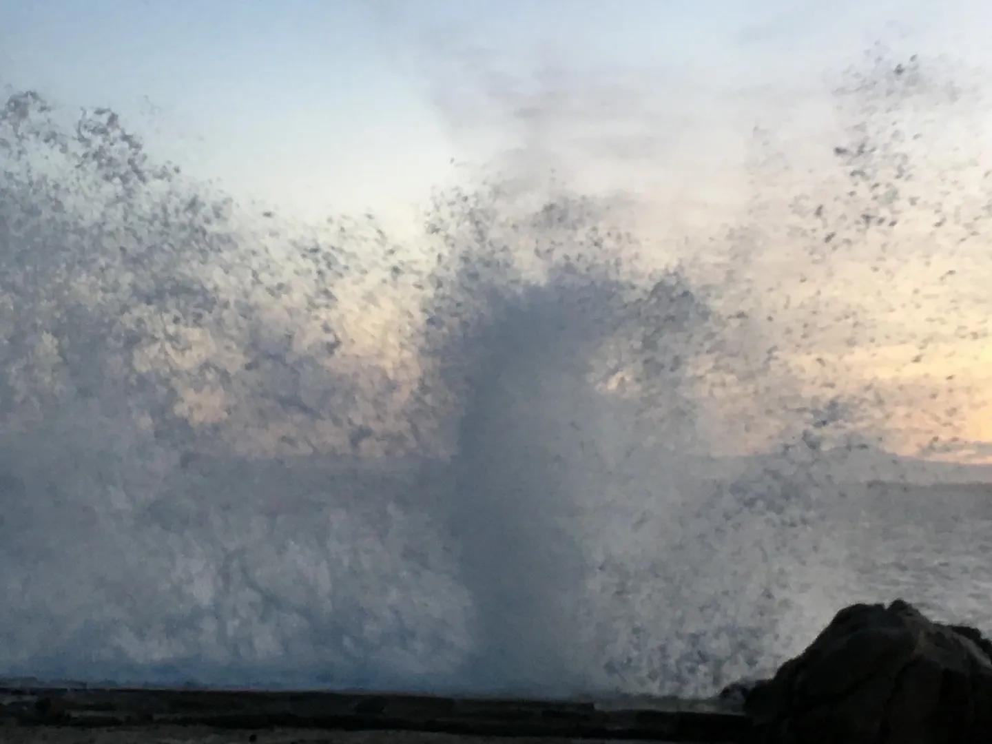 Large ocean wave crashing near the shore at sunset.