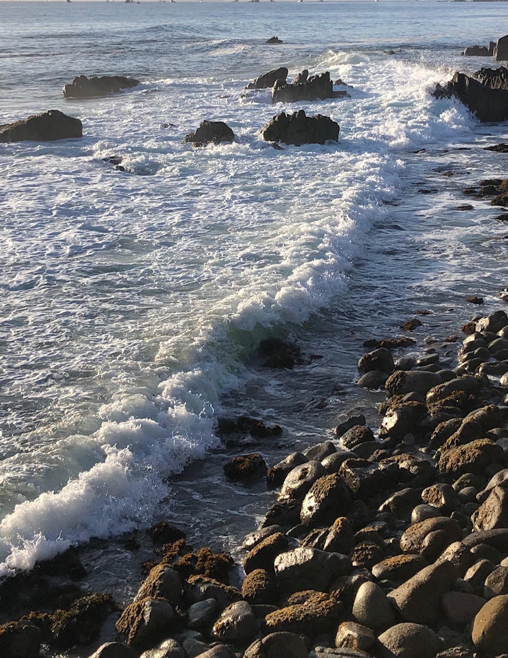 Waves crashing against rocky shoreline under soft sunlight.