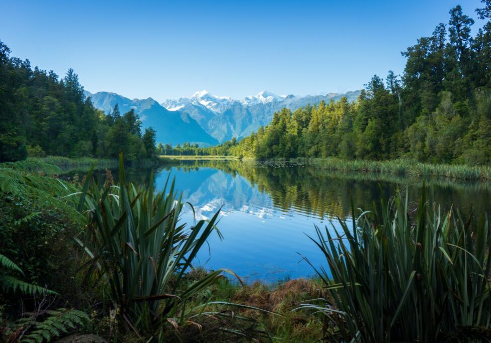 Tranquil lake reflecting snow-capped mountains and lush greenery.