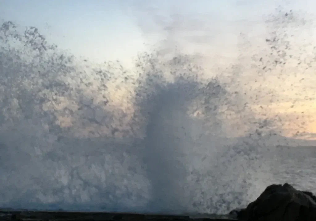Large ocean wave crashing near the shore at sunset.